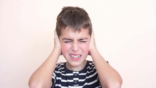 Young boy with closed eyes covering his ears with hands because of loud noise