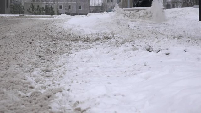 Man cleans snow from street sidewalk via snow removal machine. Closeup. 4K