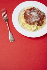 A dinner dish of spaghetti Bolognese on a bright red background with fork and blank space below