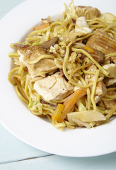 A dinner dish of chicken noodle stir fry on a blue wooden dining table background