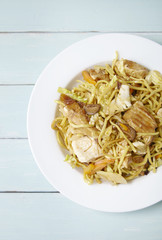 Overhead view of a dinner dish of chicken noodle stir fry on a blue wooden dining table background