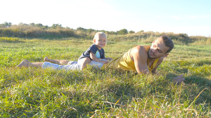 Little child goes at the field to his father, lying on green gra