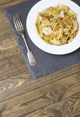 A dinner dish of chicken noodle stir fry on an old wooden table top background with fork and empty space below