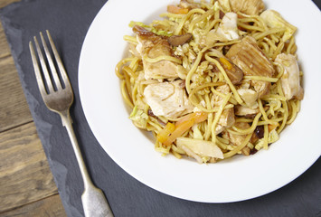 A dinner dish of chicken noodle stir fry on an old wooden table top background