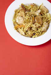 A dinner dish of chicken noodle stir fry on a bright red background with blank space below