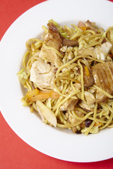 A dinner dish of chicken noodle stir fry on a bright red background