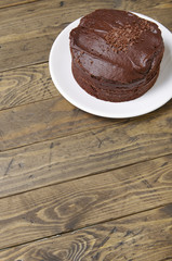 A whole chocolate fudge layer cake on a rustic wooden table top background with blank space below
