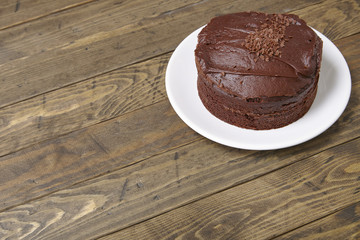 A whole chocolate fudge layer cake on a rustic wooden table top background with blank space below