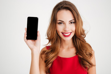 Fototapeta premium Smiling woman in red dress showing blank smartphone screen