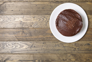A whole chocolate fudge layer cake on a rustic wooden table top background with blank space at side