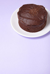 A whole chocolate fudge layer cake on a pastel purple background with blank space below