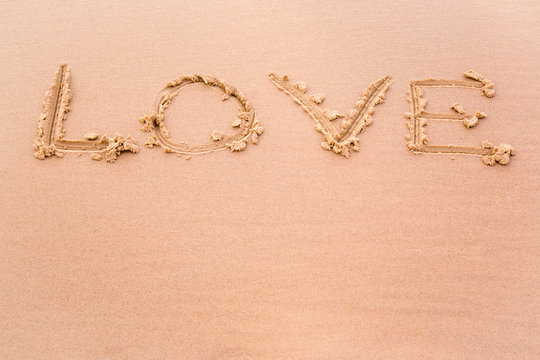 Love word drawn on wet sand by the waves on the shore. Background.