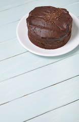 A whole chocolate fudge layer cake on a blue wooden table top background with blank space below