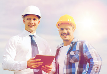 smiling builders in hardhats with tablet pc