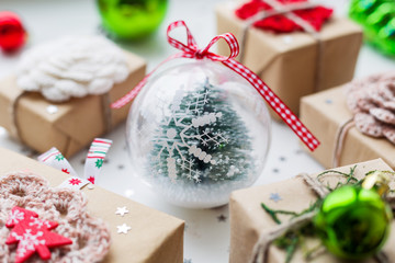 Christmas and New Year background with presents, decorations and transparent decorative ball with fir tree inside.
