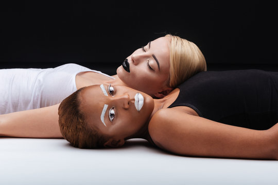Two young women with stylish makeup lying on white floor