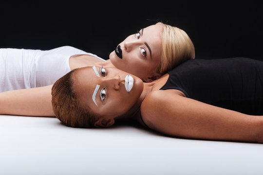 Two young women with fashion makeup lying on white floor