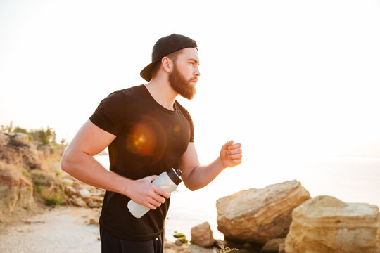 Young sporty bearded man athlete running at the rocky beach