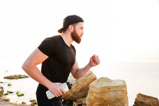 Confident young bearded man athlete running on the beach