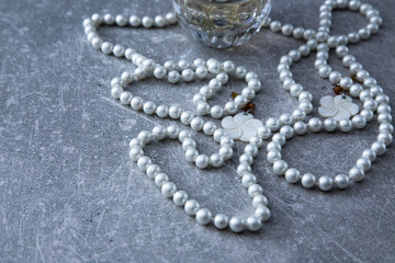 a strand of pearls and perfume on a stone background