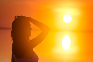 Beautiful female model enjoying sunset at seaside. Calm water of salt lake Elton reflects woman's silhouette. Sun goes behind horizon. Girl is alone