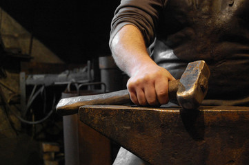 Blacksmith sitting in forge and holding hammer in hand on the anvil © annavolotkovska