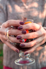 Mulled wine in woman hand on autumn leaf background. Close up. Hot christmas drink.