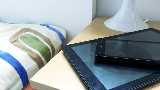 young man fall asleep in bed - smartphone and tablet on bedside table - closeup