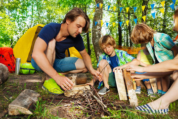 Father teaching kids to make a camp fire in forest