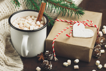 Cup with homemade Christmas hot Chocolate drink, Marshmallows and Holiday Gift on dark background. Winter time concept. Selective focus. Toned