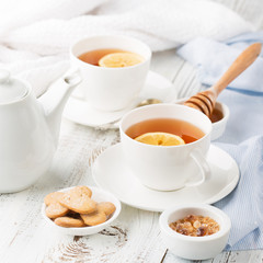 Two cups of hot black tea, lemon, homemade cookies and honey on white rustic wooden background. Selective focus