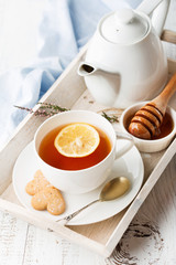 Tray with cup of hot black tea, lemon and honey on white rustic wooden background. Breakfast concept. Selective focus