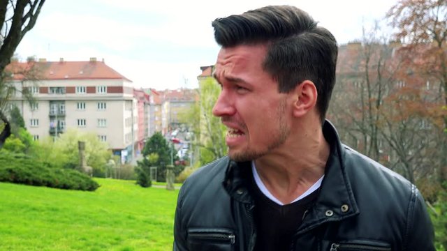 Young handsome man stands, is angry and yells in park