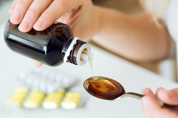 Young woman taking medicine on spoon at home.