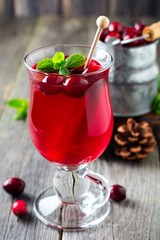 Fresh cranberry juice with cinnamon and anise in glass jars on the old wooden background. Selective focus.