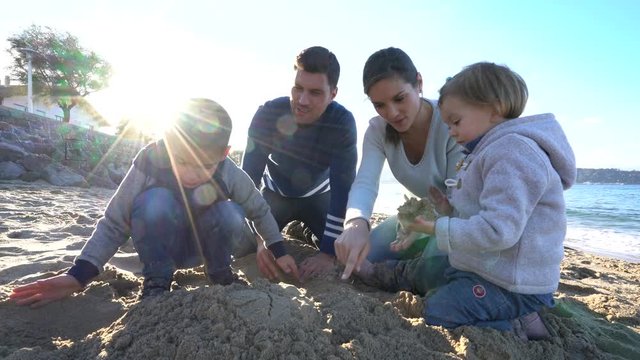 Family at the beach building up sand castle
