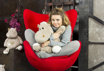 Smiling young girl sitting with soft toys on a red chair
