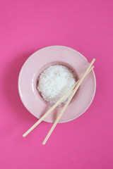 Pink plate with rice and chopsticks on the pink background