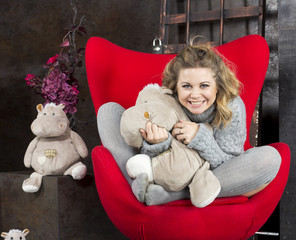 Smiling young girl sitting with soft toys on a red chair
