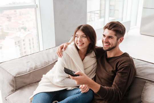 Cheerful cute young couple hugging and watching TV on couch - Powered by Adobe