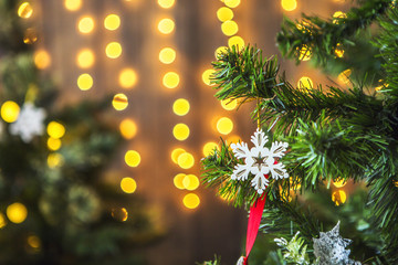 Fototapeta na wymiar Новогодняя зеленая елка, украшенная новогодними игрушками и гирляндой с желтыми огнями. На заднем фоне желтые размытые огни.