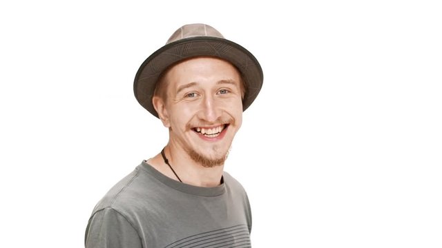 Young handsome man in hat smiling, passing by over white background. Slow motion.