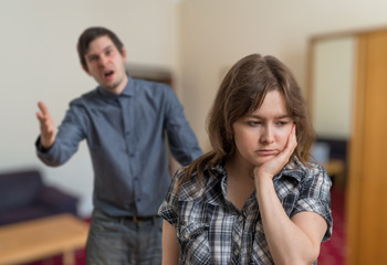 Fototapeta premium Young couple is arguing. Angry man is explaining something and shouting. Sad woman is ignoring him.