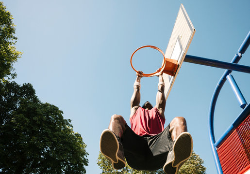 Young male basketball player hanging from basketball hoop