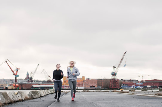 Two female running friends running along dockside