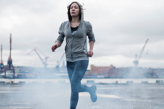 Young female runner running  on stormy dockside