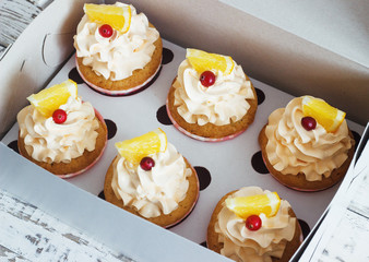 Vanilla cupcakes with a cap of cream on white wooden tablein the box