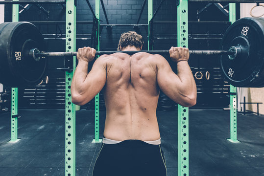 Rear view of male cross trainer weightlifting barbell in gym