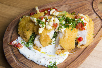 Crispy fried chicken with, tomato, cheese, ruccola, cream on wooden background