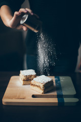 Woman hands sprinkle cake with powdered sugar
